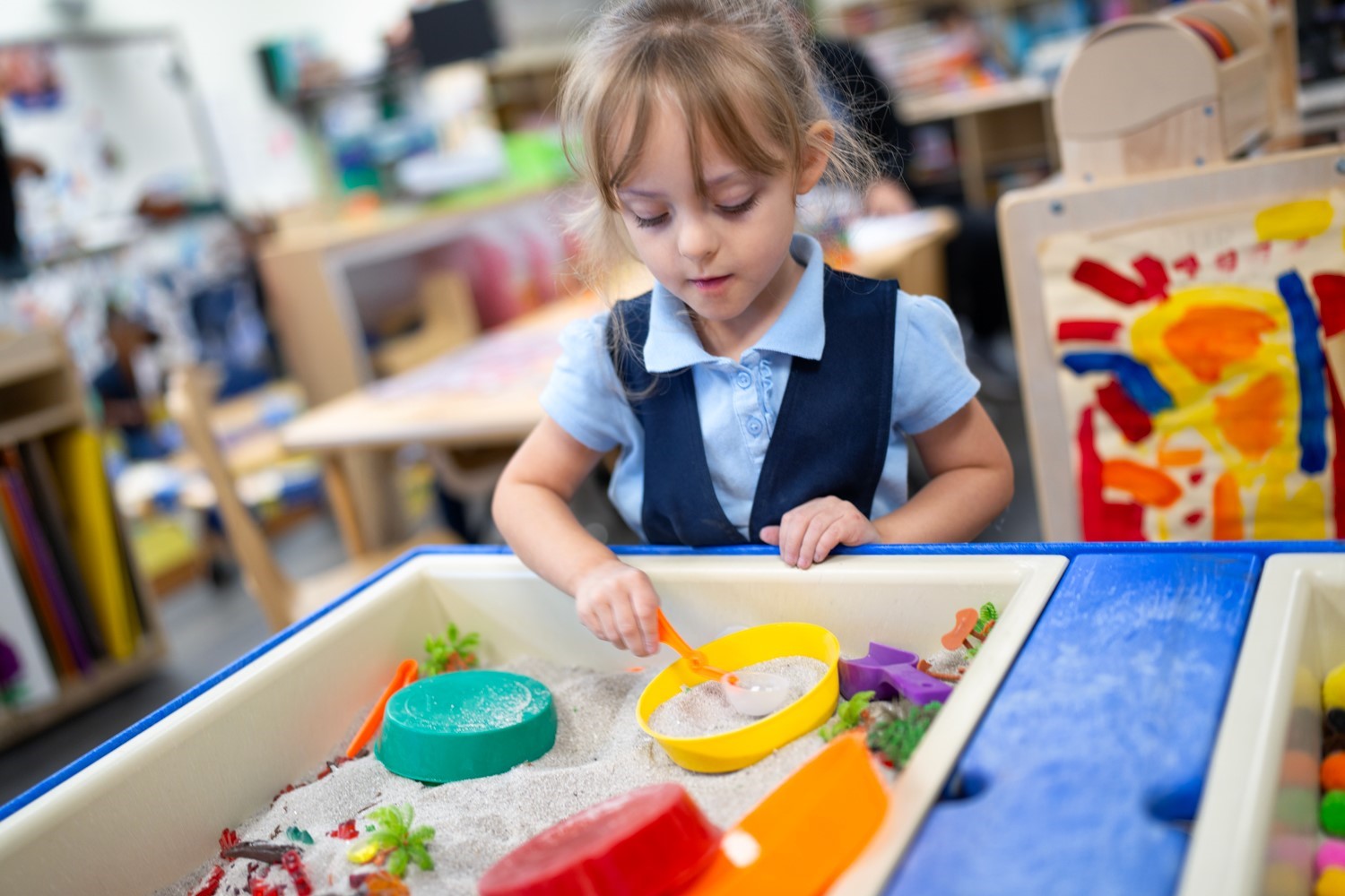 A young girl plays with toys in a sandbox located in a clean and engaging pre-K classroom.