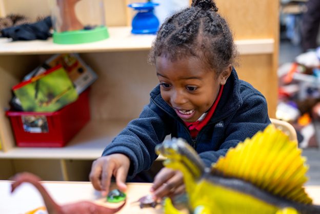 A young girl enjoying playing with dinosaur toys at a table in a nice preschool classroom.